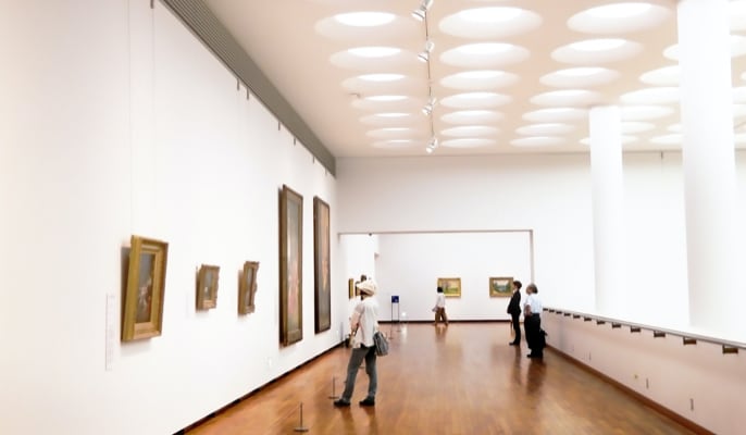 Vast gallery with tall ceiling showing several people walking around viewing art hanging on the wall