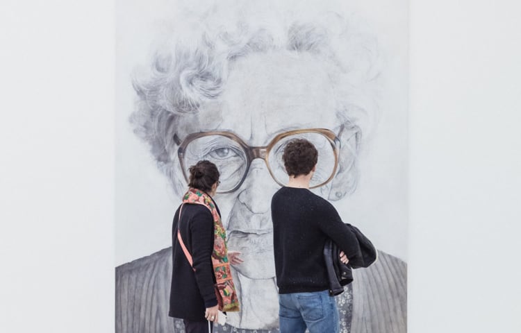 A couple walking and viewing a large profile image of an older woman in glasses